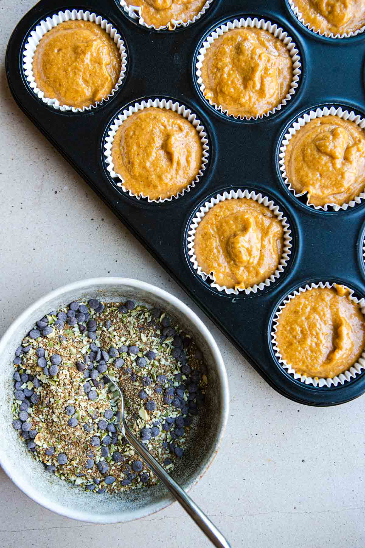 dark chocolate and pepita streusel in a white bowl next to protein muffin batter