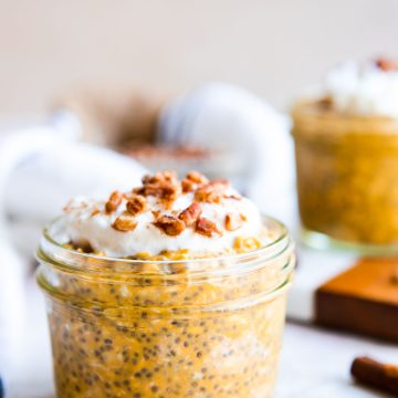 an 8 ounce mason jar filled with pumpkin protein oats and topped with a bit of whipped cream and crushed pecans