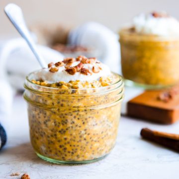 a small mason jar with pumpkin spice overnight oats and garnished with whipped cream and pecans