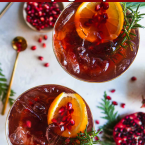 2 champagne glasses filled with a pomegranate champagne cocktail and garnished with rosemary and orange slices