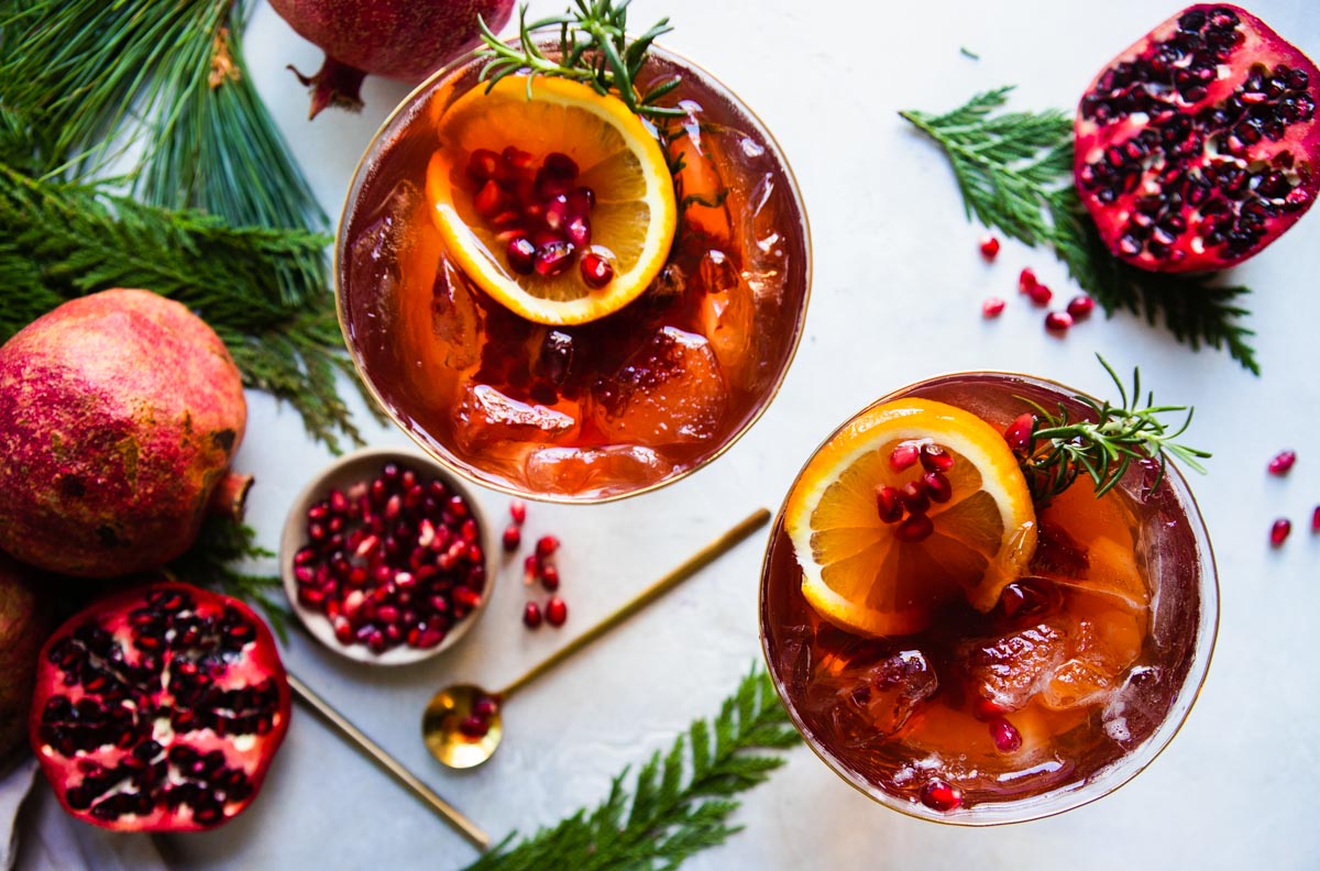 2 pink champagne flutes filled with a pomegranate champagne spritz and garnished with orange slices and pomegranate aerials.