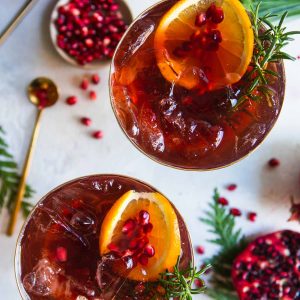 2 champagne flutes filled with a pomegranate spritz cocktail and garnished with rosemary and orange slices