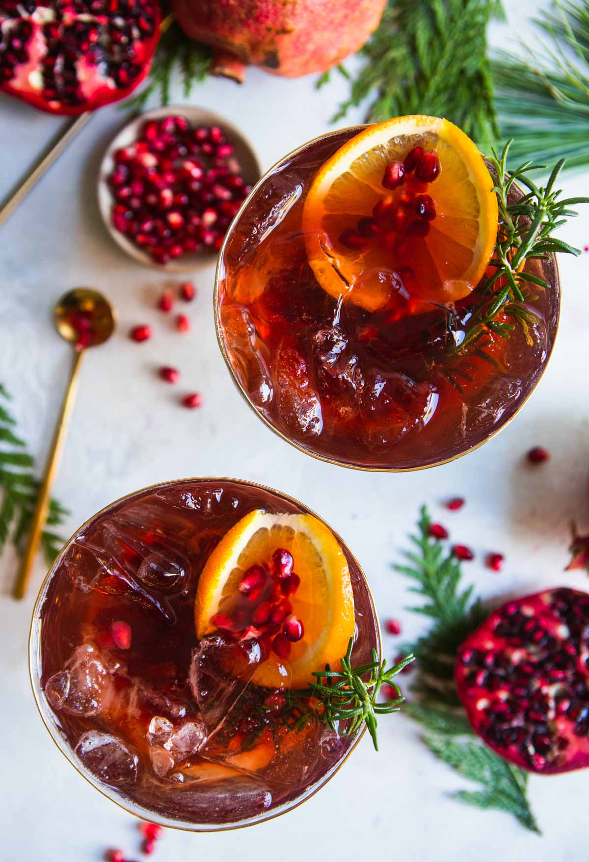 2 champagne flutes filled with a pomegranate spritz cocktail and garnished with rosemary and orange slices 