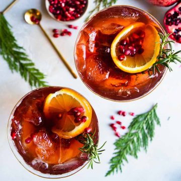 fir branches next to pomegranates and cocktail glasses filled with a champagne spritzer