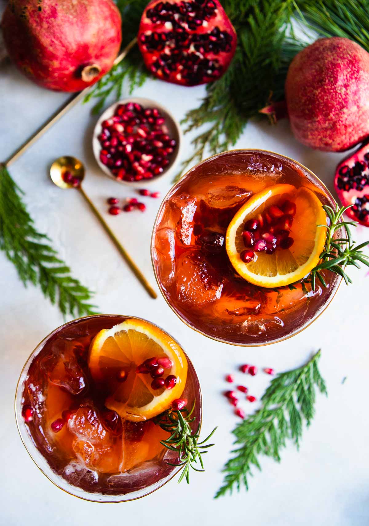 pomegranates cut up and placed next to 2 glasses filled with pomegranate spritz cocktails 