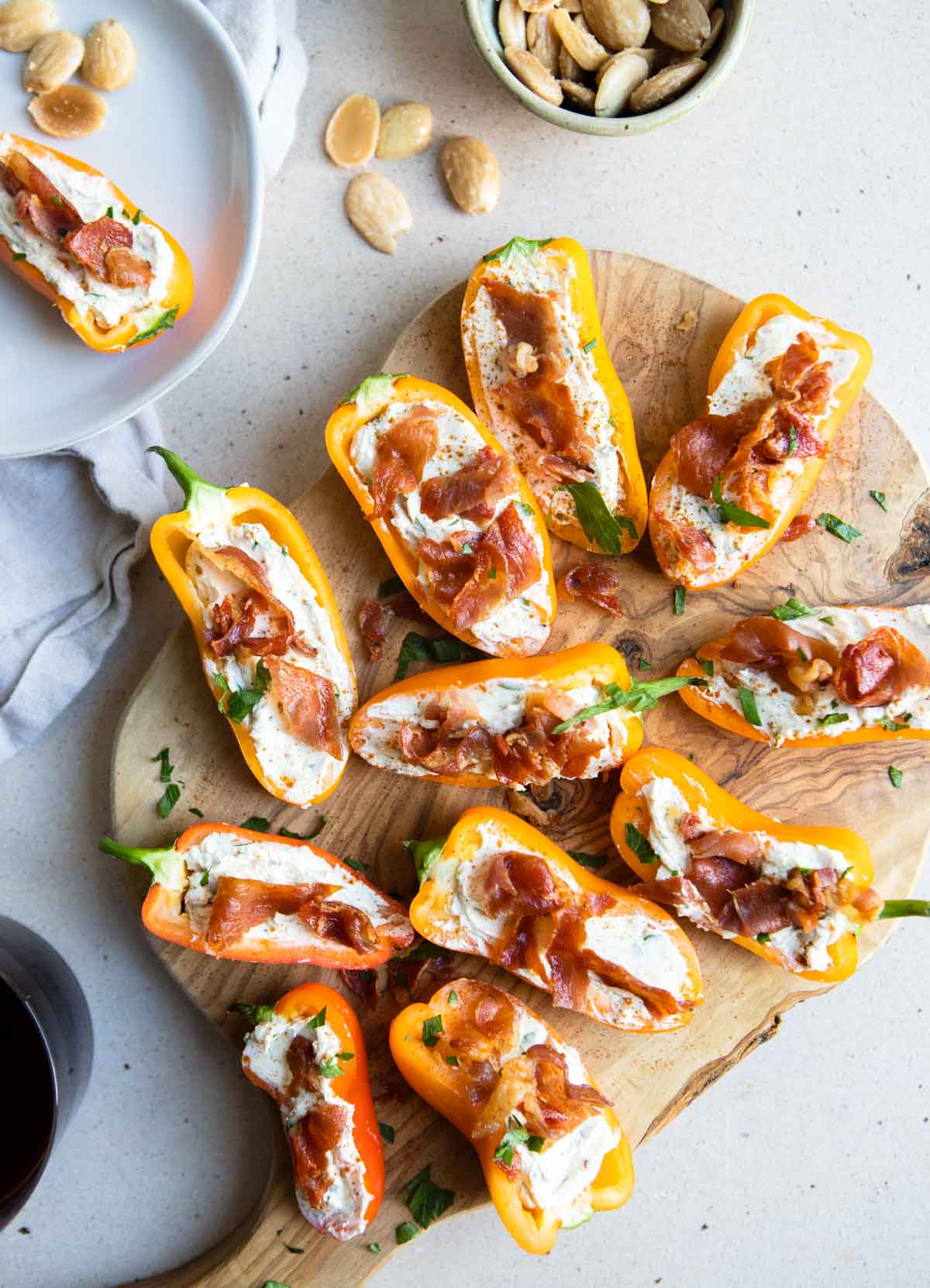 mini peppers stuffed with goat cheese and garnished with crispy prosciutto on a wood cutting board 