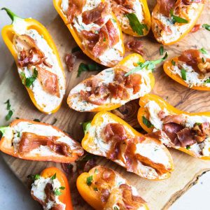 goat cheese stuffed mini peppers topped with crispy prosciutto on a wood cutting board