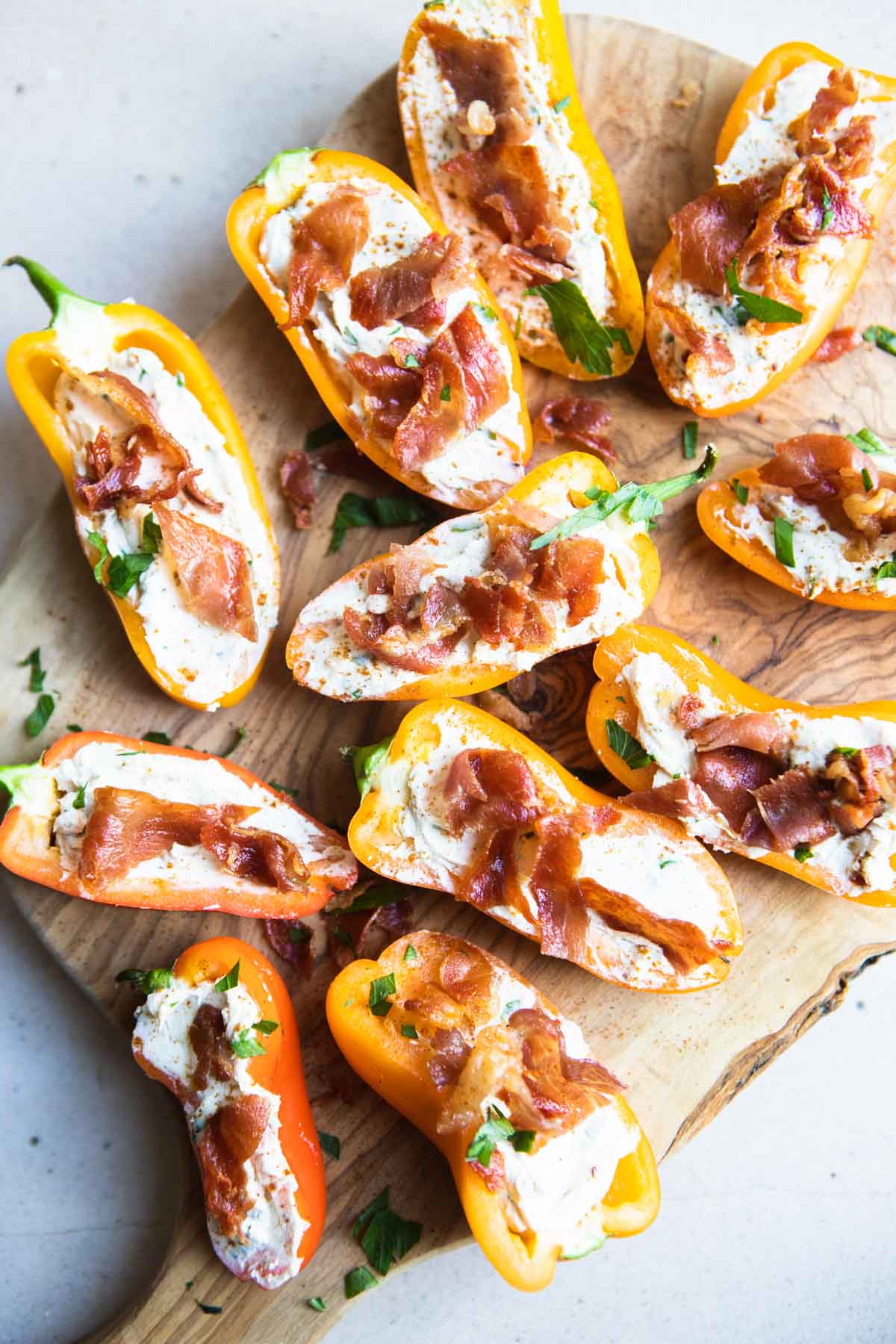 goat cheese stuffed mini peppers topped with crispy prosciutto on a wood cutting board