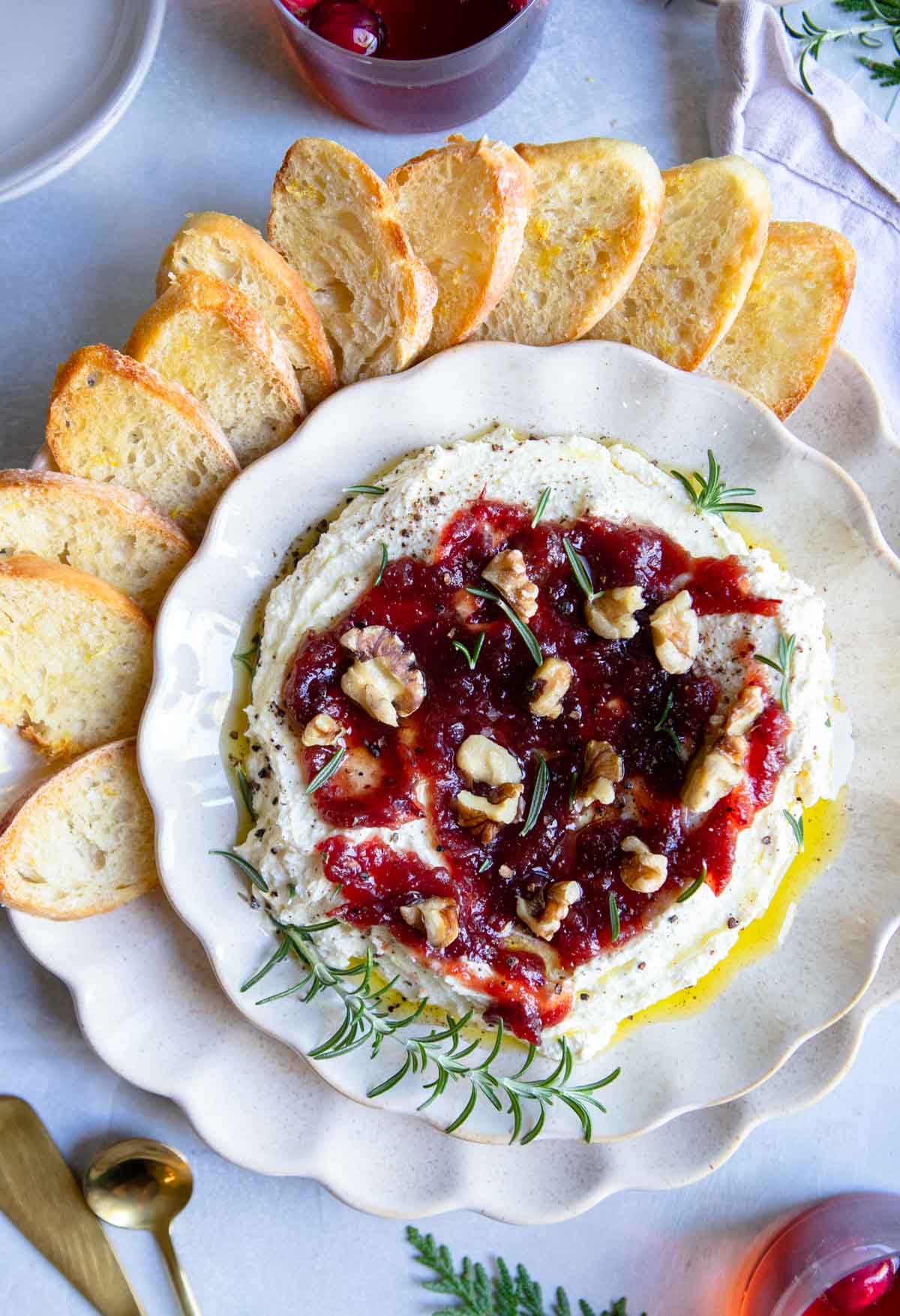 scalloped plate filled with whipped feta dip and topped with cranberry sauce and garnished with rosemary and walnuts 