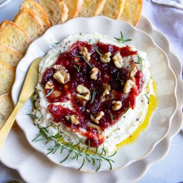 cranberry whipped feta dip on a cream scalloped plate and set next to crostini