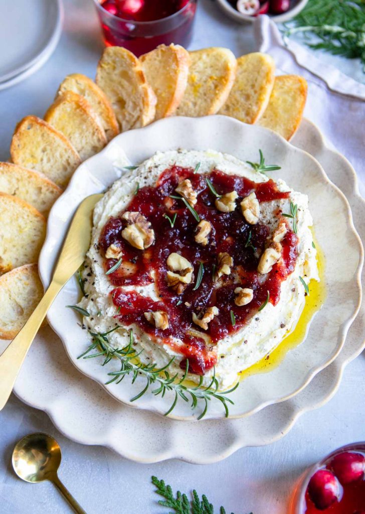 a scalloped plate holding a whipped feta dip with cranberry sauce and crostini