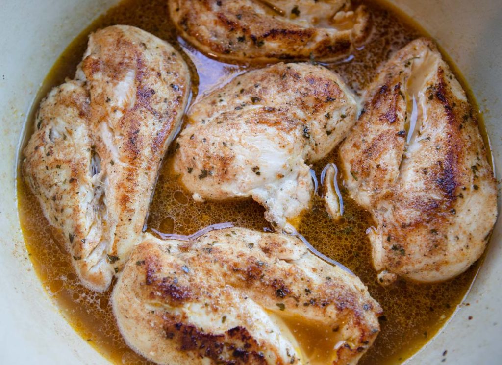 chicken breasts submerged in chicken broth in a Dutch oven