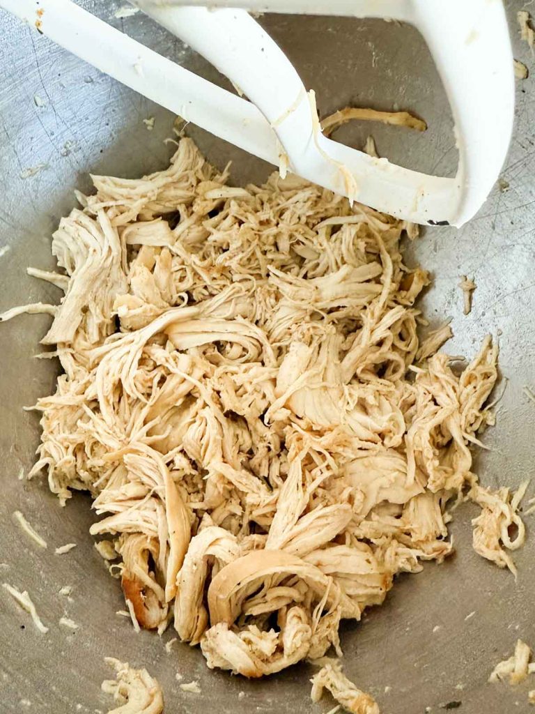 shredded chicken breasts in the bowl of a stand-up mixer.