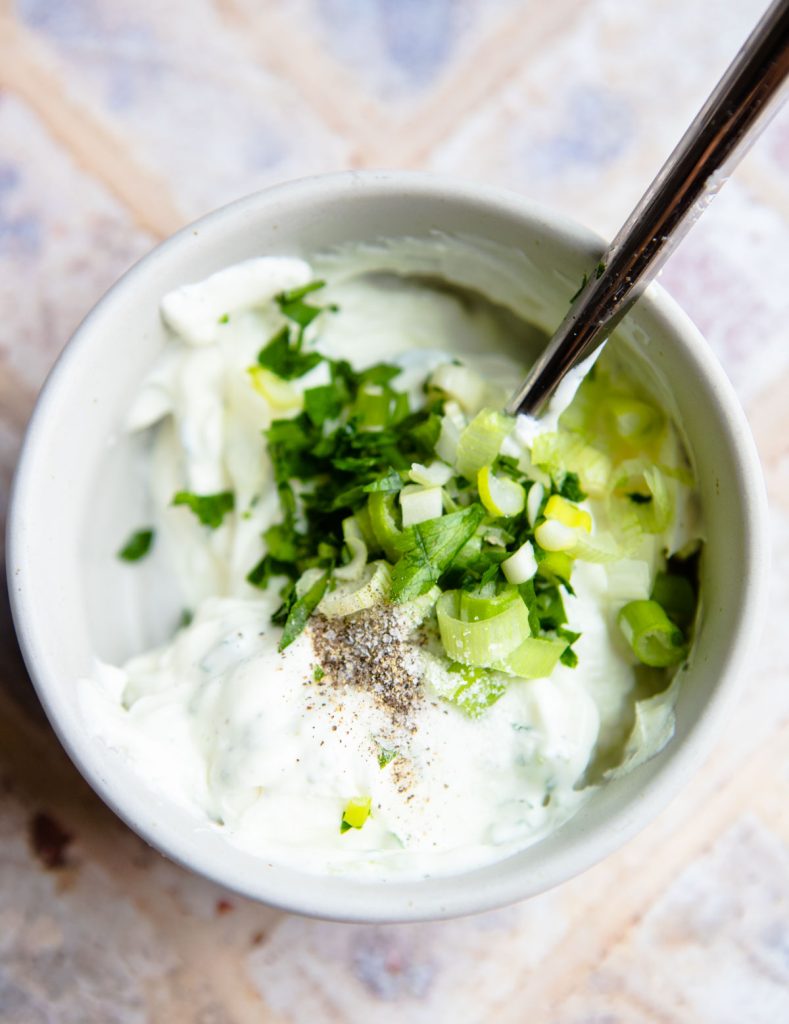 Greek yogurt and fresh herbs and green onion in a white ceramic bowl