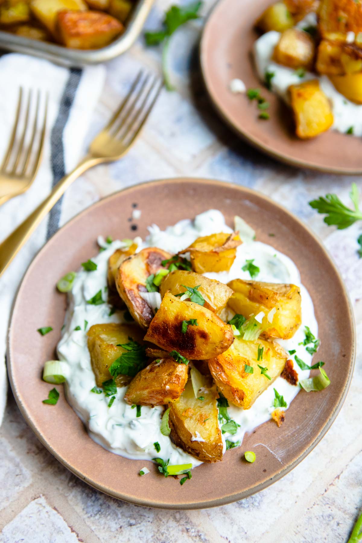 2 brown plates filled with roasted baby dutch yellow potatoes and layered with a savory Greek yogurt sauce