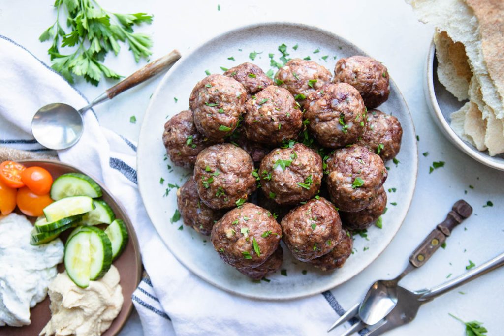 lamb and beef meatballs on a gray plate next to fresh cut veggies and pita bread