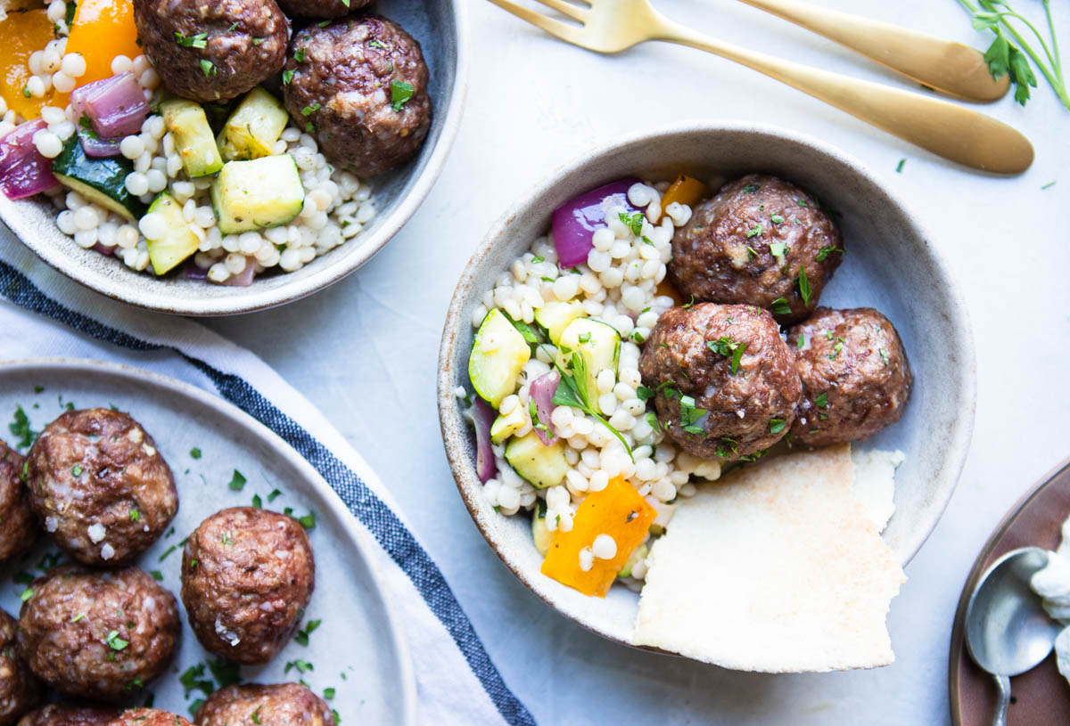 2 bowls filled with a pearl couscous salad and topped with Greek lamb meatballs 