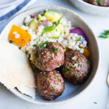 ceramic bowl filled with couscous salad and lamb and beef meatballs