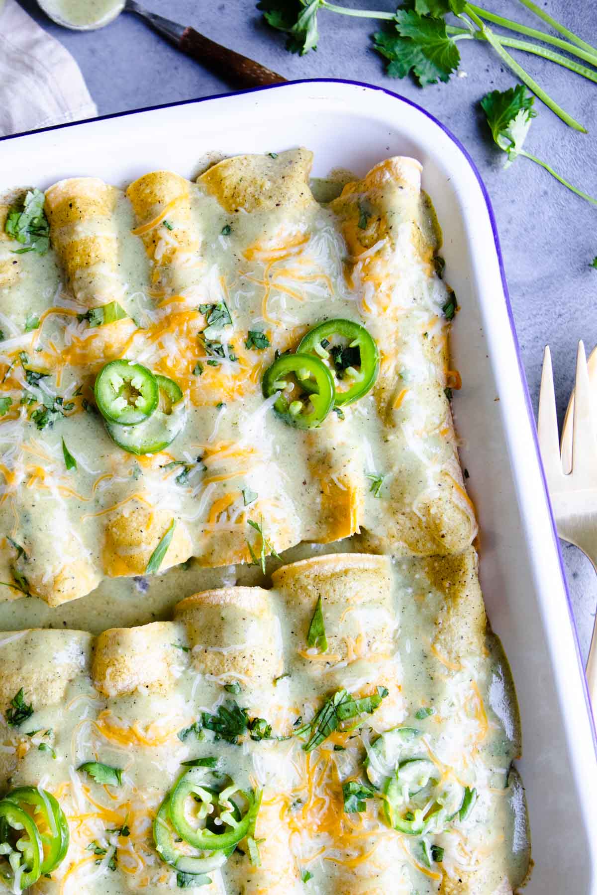 a white baking dish filled with green chili chicken enchiladas 