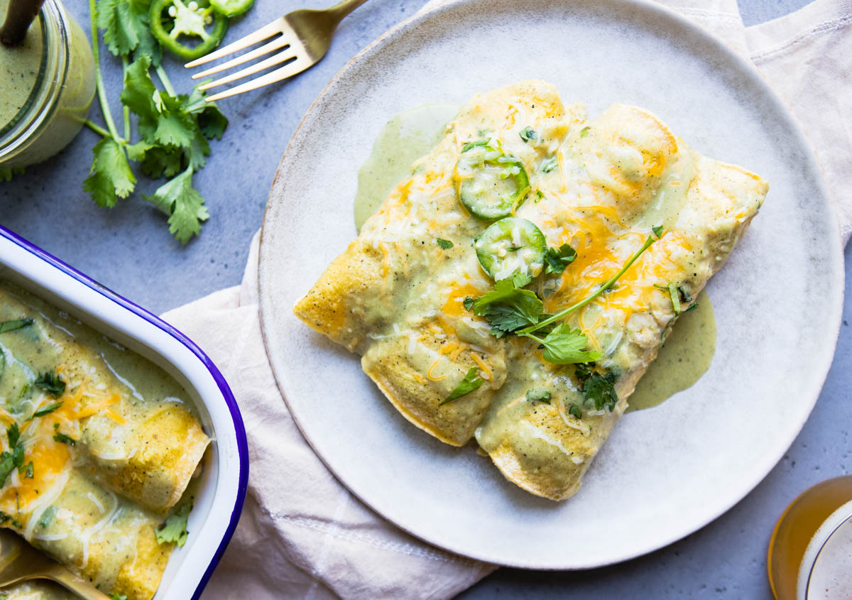 a ceramic plate with 3 healthy chicken enchiladas set on top and smothered with homemade green enchilada sauce