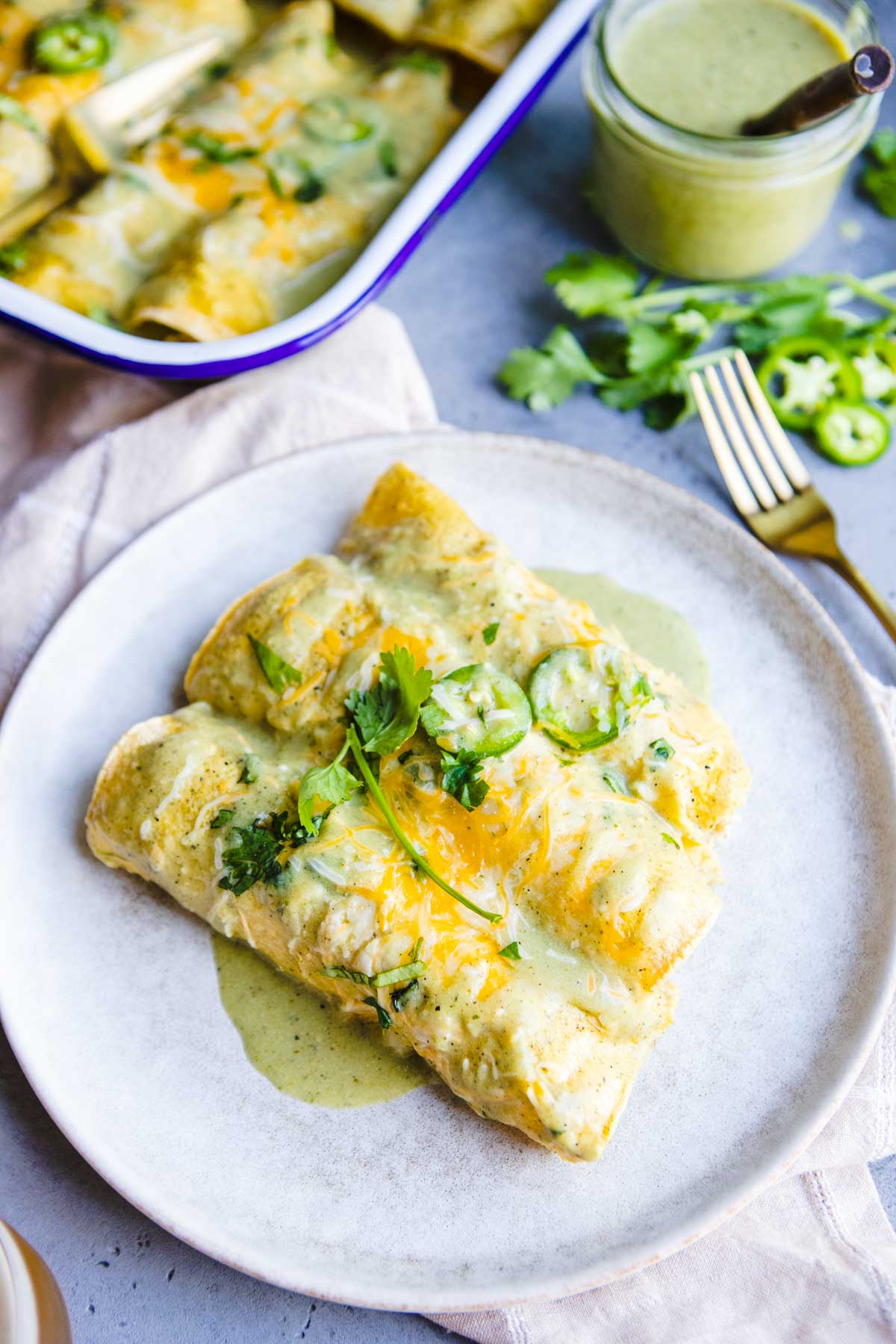 ceramic plate topped with healthy chicken enchiladas and topped with green sauce and cheese