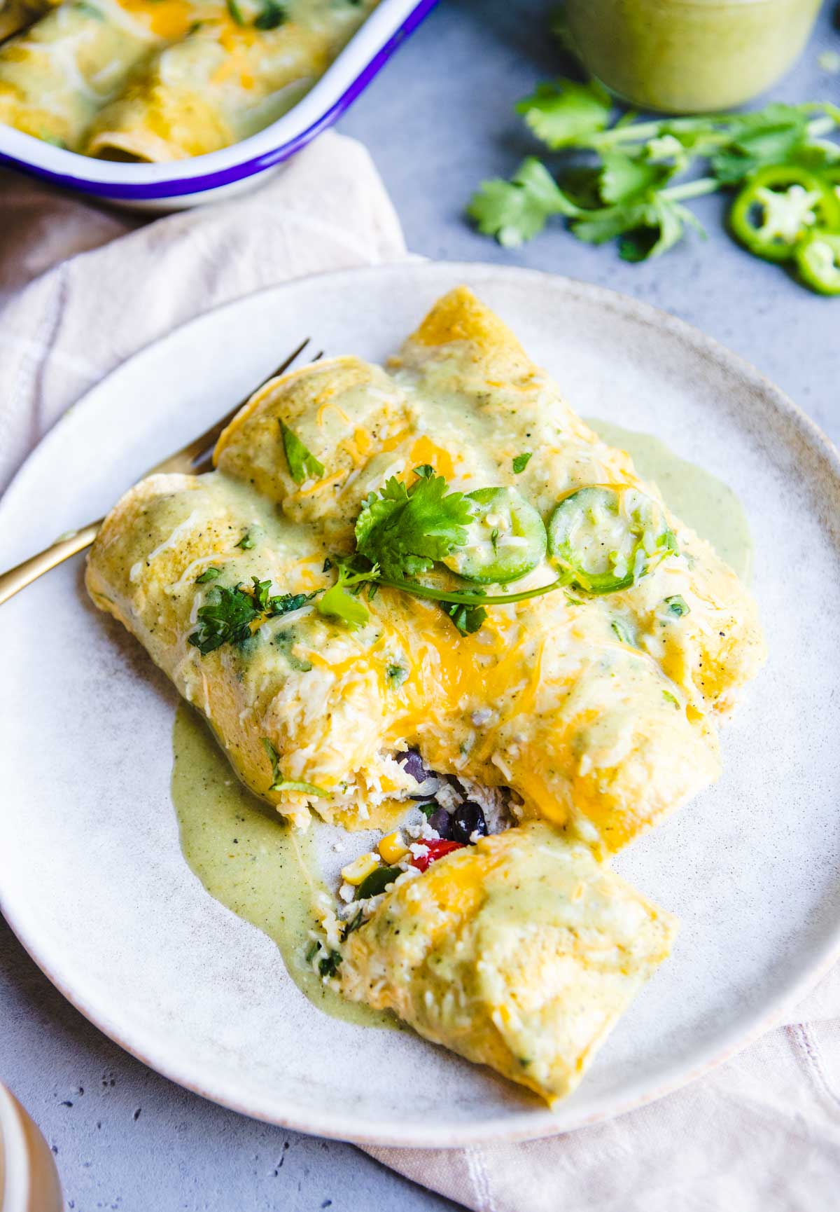 3 chicken enchiladas stuffed with veggies on a plate and topped with green chili sauce