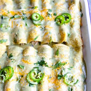 a white ceramic baking dish filled with healthy green chili chicken enchiladas