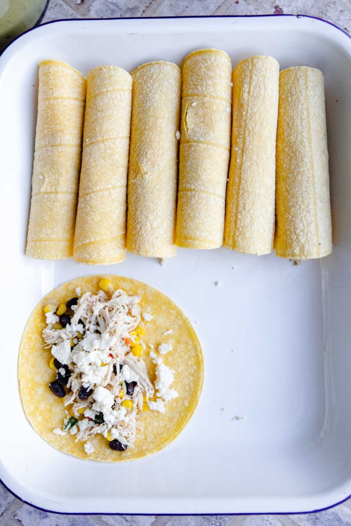 corn tortillas in a casserole dish filled with chicken and veggies to make enchiladas 