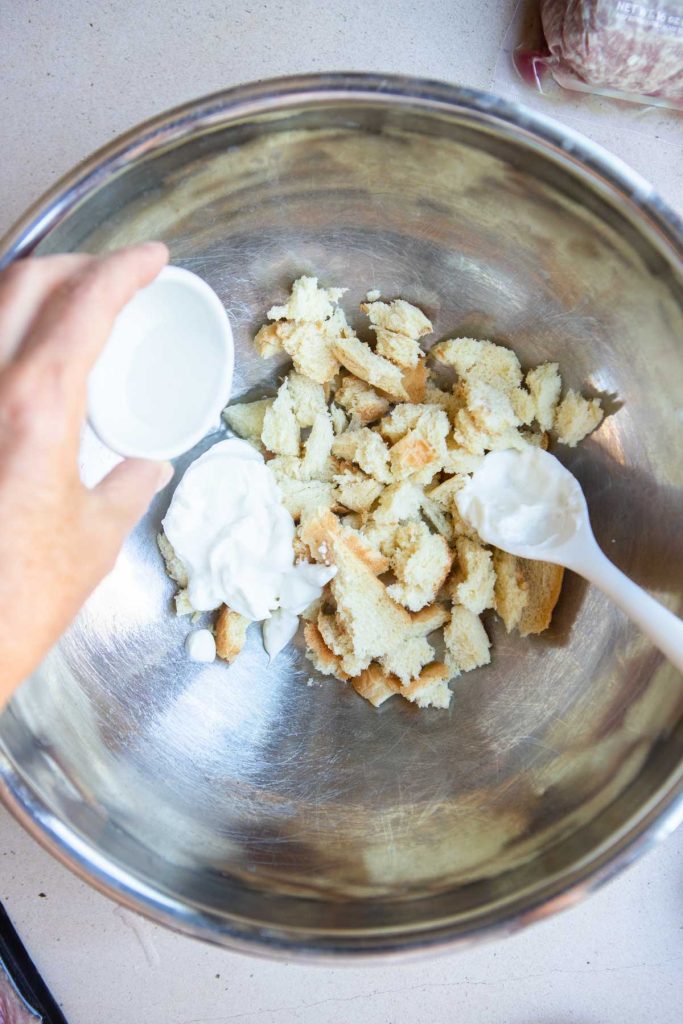 torn pieces of bread, Greek yogurt and water in a stainless mixing bowl