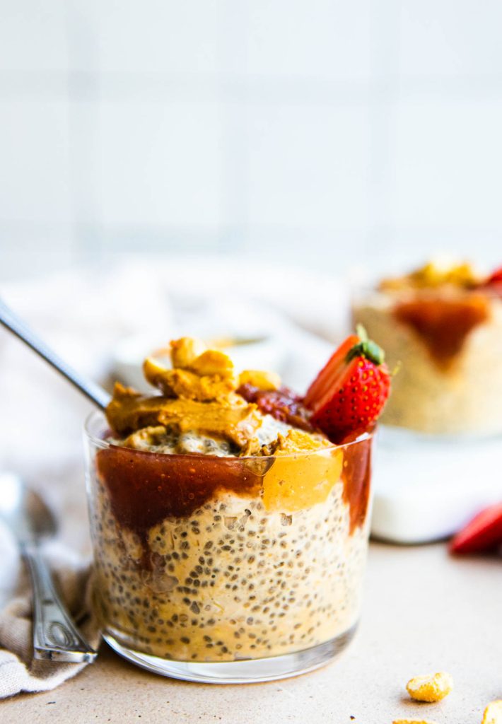 a glass cup filled with peanut butter and jam overnight oats and topped with fresh strawberries