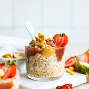 2 glasses filled with healthy peanut butter overnight oats and topped with strawberry jam and fresh strawberries