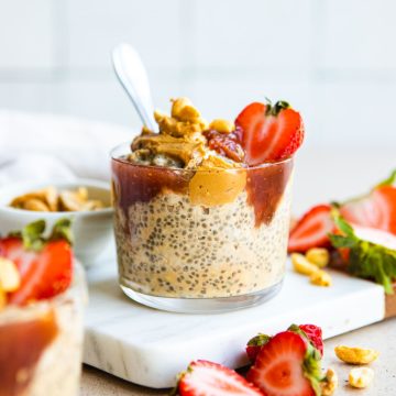 glass cup filled with peanut butter and jelly overnight oats topped with fresh strawberries and peanuts