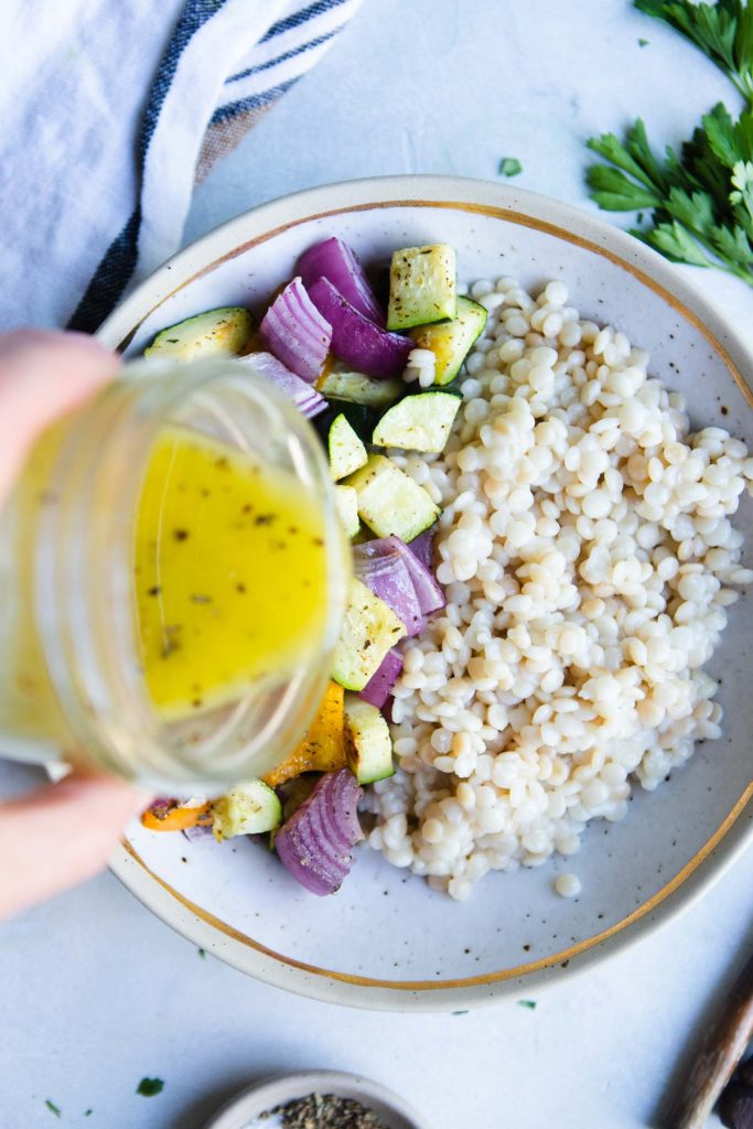 vinaigrette dressing being added to a pearl couscous with vegetables dish