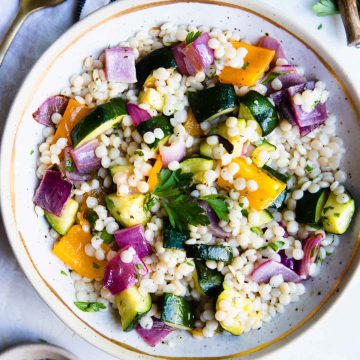 couscous with vegetables served in a beige plate and garnished with fresh parsley