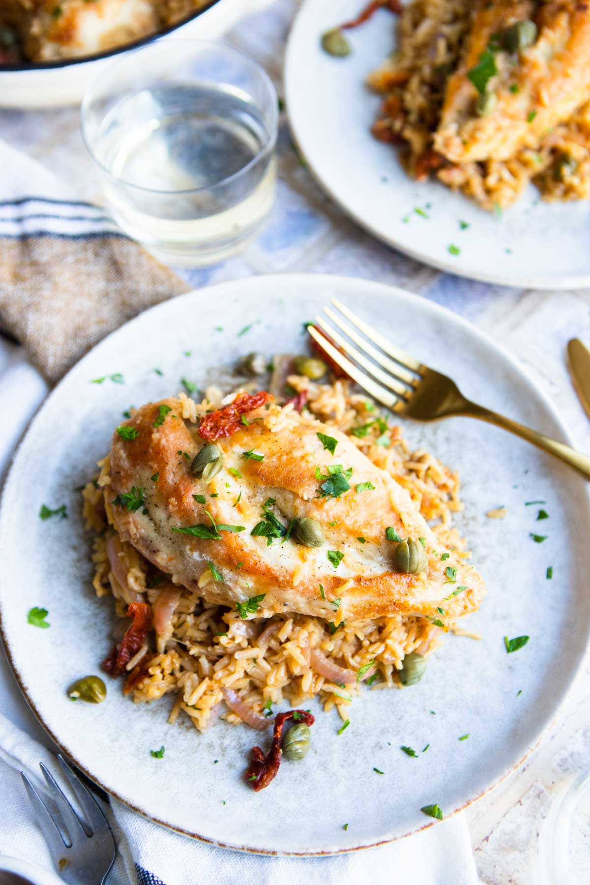 2 beige ceramic plates filled with an herbed rice and a seared chicken breast and garnished with capers and parsley