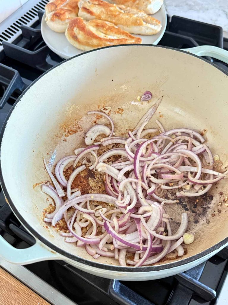 sliced red onions being seared in a large pan