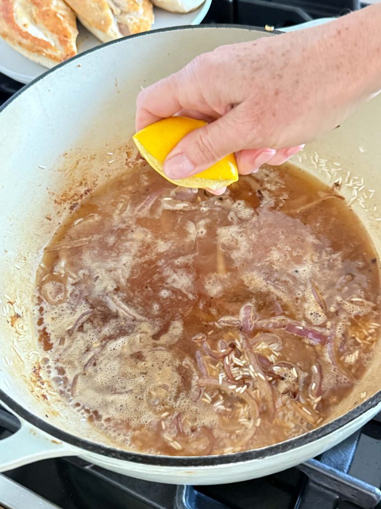 broth added to a pot of rice and aromatics and fresh lemon being squeezed into it 