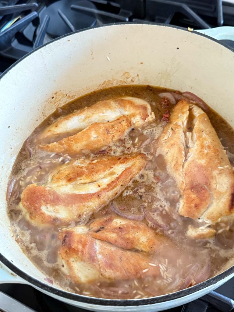 chicken breasts added to a pot of chicken broth and rice to make Mediterranean chicken and rice