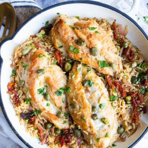 Mediterranean Chicken and Rice one pan meal made in a white cast iron skillet and garnished with capers and parsley