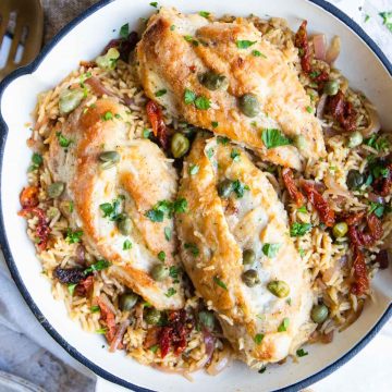 white cast iron skillet with chicken breasts and rice garnished with capers