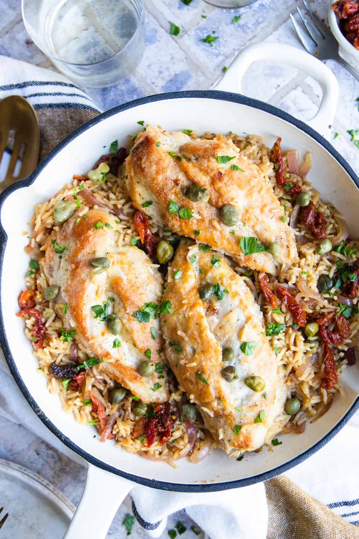 Mediterranean Chicken and Rice one pan meal made in a white cast iron skillet and garnished with capers and parsley