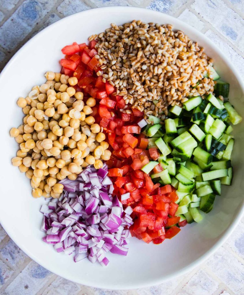 farro, garbanzo beans and veggies in a large white bowl to make a Mediterranean chopped salad