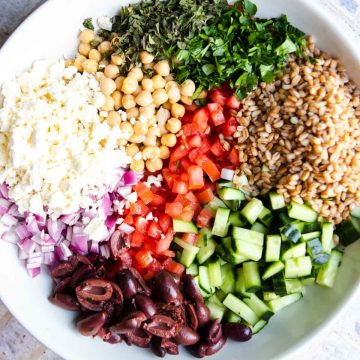 large white serving bowl with fresh veggies, beans, olives and feta cheese inside to make a Mediterranean chopped salad