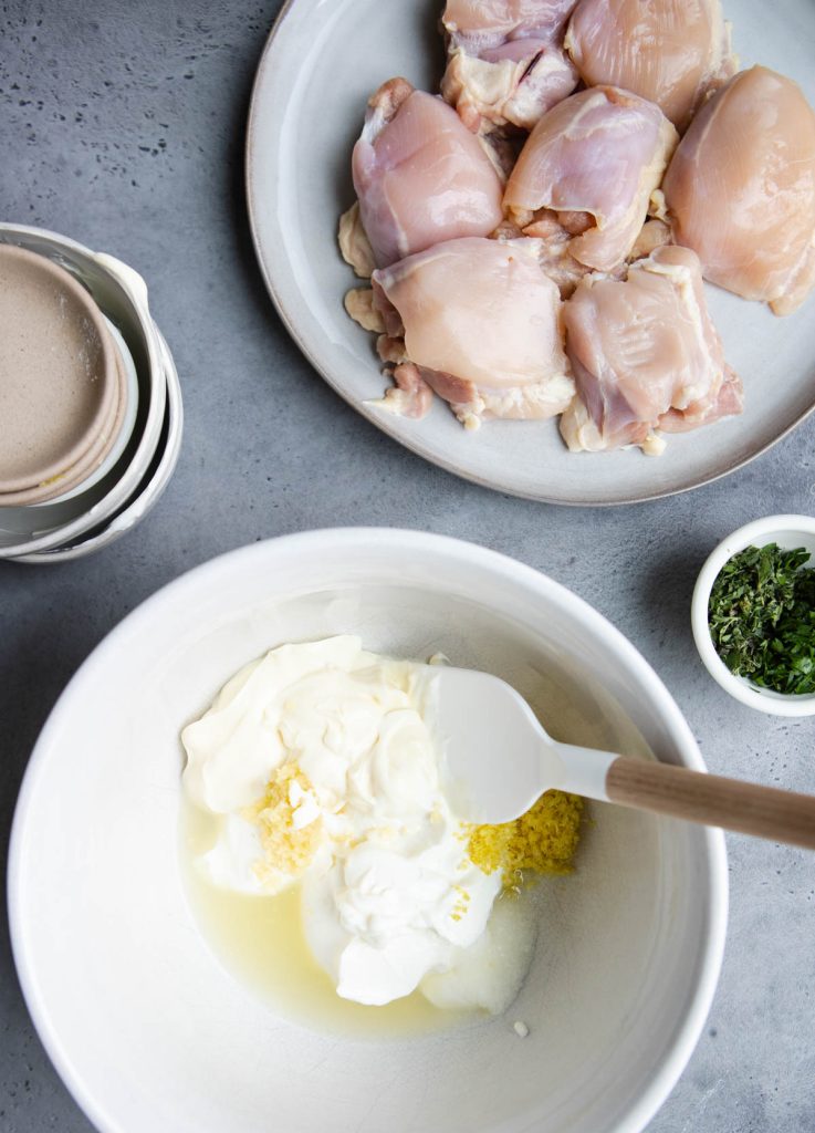 raw chicken thighs on a plate and greek yogurt marinade in a white mixing bowl