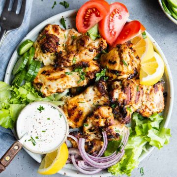 greek yogurt chicken thighs grilled on a plate with tomatoes and lemon garnish and greek dressing