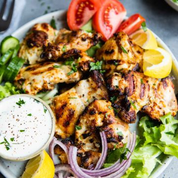 gray plate filled with greens and garnishes, and topped with Greek chicken thighs