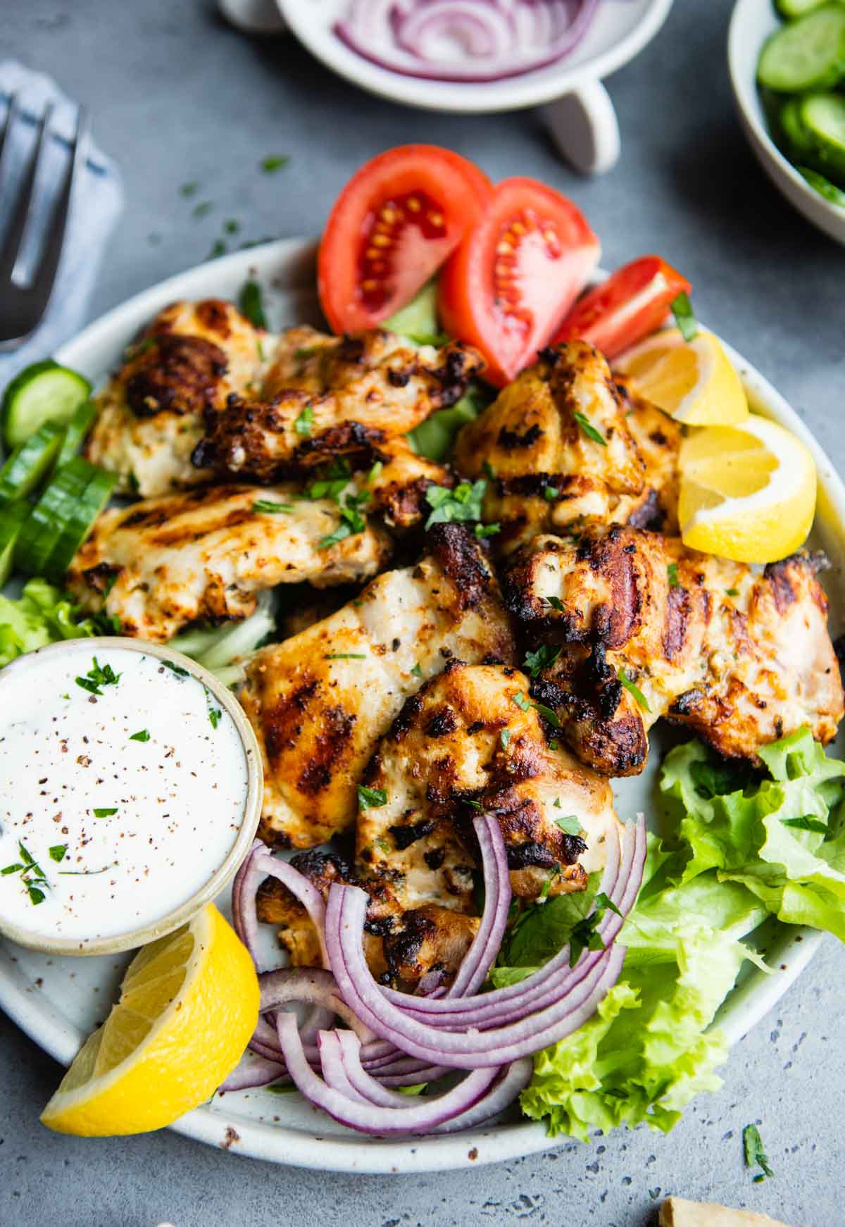 gray plate filled with greens and garnishes, and topped with Greek chicken thighs